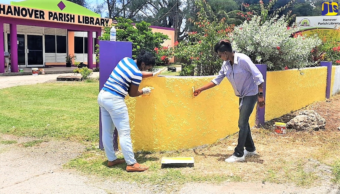 Lucea Deputy Mayor, Councillor Andria Dehaney-Grant (right), and Acting Senior Librarian for Hanover Parish Library, Ms Vonnette Jones, paint wall of Library  on Labour Day (May 23). 