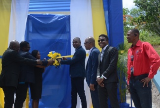 Minister of State in the Ministry of Finance and the Public Service and Member of Parliament for St. Ann South Western, Hon. Zavia Mayne (centre), cuts the ribbon to officially open a multipurpose building in Watt Town, St. Ann, on Friday (June 14). He is assisted by (from left) Deputy Mayor of St. Ann, Councillor Cardell Wickham; Executive Director Tourism Product Development Company Limited (TPDCo), Wade Mars; Director, Constituency Development Fund (CDF), Kedesha Rochester; Postmaster General, Jamaica Post, Lincoln Allen; Legal Officer and Corporate Secretary, Universal Service Fund (USF), Charles Young; and Senior Project Officer, Jamaica Bauxite Institute (JBI), Wesley Harley.
