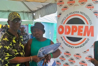 Minister of Local Government and Community Development, Hon. Desmond McKenzie (left), hands over hurricane straps and a tarpaulin to Pearl Drummond from Crawford in St. Elizabeth. Occasion was the Ministry’s Hurricane Roof Strap Expo held at the JAG Myers Park in Black River on Friday (July 26).
