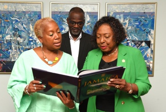 Minister of Culture, Gender, Entertainment and Sport, Hon. Olivia Grange (right) and McMaster University Professor, Dr. Juliet Daniel (left), peruse a publication on Jamaica, during a courtesy call at the Ministry’s offices in Kingston on Tuesday (March 11). Sharing in the moment is Permanent Secretary, Denzil Thorpe.

