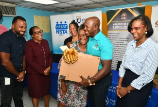 Minister of Labour and Social Security, Hon. Pearnel Charles Jr. (second right) embraces Lorraine Barnes as he presents her with a laptop during a ceremony at the National Council for Senior Citizens (NCSC) office in Kingston on Friday (May 9). Ms. Barnes was one of eight high performers in a digital literacy course offered to senior citizens by the HEART NSTA/Trust. Sharing the moment (L-R ) are Chief Executive Officer (CEO) of the Universal Service Fund (USF), Charlton McFarlane; Deputy Managing Director, National Training & Programmes Division at HEART NSTA/Trust, Dr. Cheryl McLaughlin; NCSC Chair, Dr. Julian McKoy-Davis; and Permanent Secretary in the Ministry, Dione Jennings.