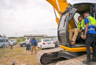 Prime Minister, Dr. the Most Hon. Andrew Holness, operates an excavator during the ceremony to break ground for the $2.4-billion Naggo Head to Braeton Road Project in Portmore, St. Catherine, on Wednesday (June 25). He is assisted by excavator operator with project contractors S&G Road Surfacing Materials Limited, Giovanni Chatterpaul. The four-lane expansion is being implemented under the Government’s Capital Expenditure (CAPEX) Programme.