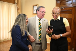 Science, Energy, Telecommunications and Transport Minister, Hon. Daryl Vaz (centre), shares something on his phone with Minister of Education, Skills, Youth and Information, Senator Dr. the Hon. Dana Morris Dixon (left), and Minister of Finance and the Public Service, Hon. Fayval Williams, at a special press conference on Tuesday (July 1), at Jamaica House.


