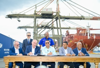 Prime Minister, Dr. the Most Hon. Andrew Holness (seated, centre), signs the Westlands Expansion Project agreement during a ceremony held at Kingston Freeport Terminal Limited (KFTL), Port Bustamante, Kingston, on Thursday (July 10).  Other signatories include (from left, seated) Chief Executive Officer, KFTL, Captain Jedrzej Mierzewski; Senior Vice President, CMA Terminals Holding, Emmanuel Delachambre; Port Authority of Jamaica (PAJ) Chairman, Alok Jain, and President and Chief Executive Officer, Professor Gordon Shirley. Among those looking on is Minister of Industry, Investment and Commerce, Senator the Hon. Aubyn Hill (standing right).

