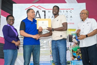 Prime Minister, Dr. the Most Hon. Andrew Holness (second left) presents White House, Westmoreland resident Wayne Parry (second right) with his land title, during a ceremony hosted by the Housing Agency of Jamaica (HAJ), at the Hotel Comingle in Savanna-la- Mar on Friday ( July 18) . Looking on (from left) are Managing Director of the HAJ, Doreen Prendergast and HAJ Chairman, Norman Scott. 