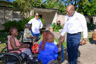 Minister of Labour and Social Security, Hon. Pearnel Charles Jr (right), engages with residents of Cheshire Village, during a visit to the community for disabled persons in St. Andrew last December to hand over care packages.  Looking on is State Minister, Dr. the Hon. Norman Dunn.